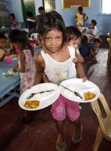 A girl carrying her younger sister on her back collects their free meals during a feeding program at a slum area in Baseco, Tondo city, metro Manila May 22, 2013. (MNS photo)